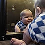 baby, infant, child, mirror, mirror_reflection, smiling, checkered_shirt, blue_clothing, chubby_cheeks, toes, foot, arm, head, back_of_head, indoor, lamp, low_light, portrait, playful, bed
