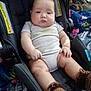 baby, infant, car_seat, onesie, knitted_booties, chubby_legs, face, hands, head, portrait, indoor, blanket, backpack, bag, safety_label, seat, striped_clothing, cozy, neutral_expression, sitting