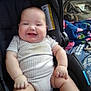 baby, infant, smiling, car_seat, onesie, chubby, cheeks, hands, legs, blanket, backpack, buckle, seat_pad, portrait, indoors, happy, clothing, plush_blanket, diaper, sitting