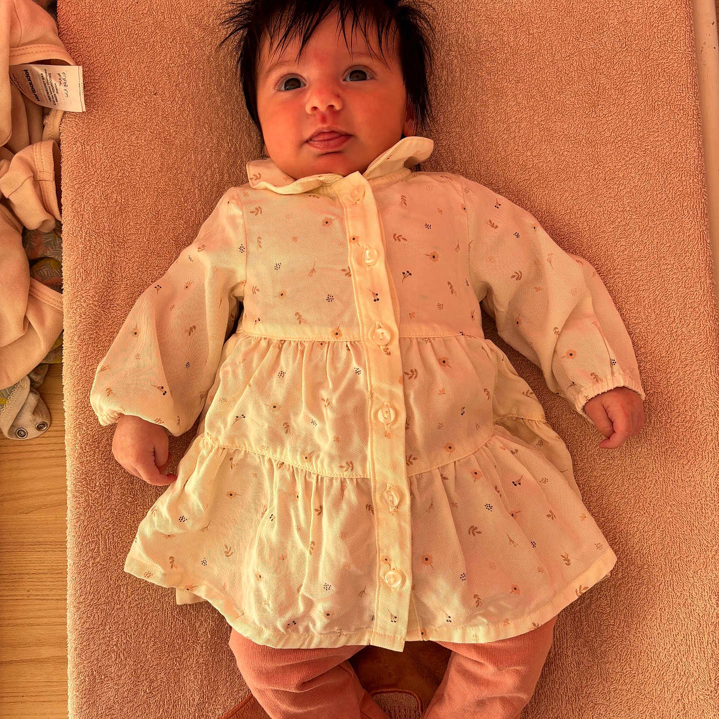 Iris a rejoint le concours — aidez-le/la à gagner de superbes lots ! baby, child, clothing, cute, dress, fabric, face, floral_pattern, foot, hair, hand, indoor, infant, lying_down, pink_pants, skin, soft_texture, tongue_out, towel, wooden_surface