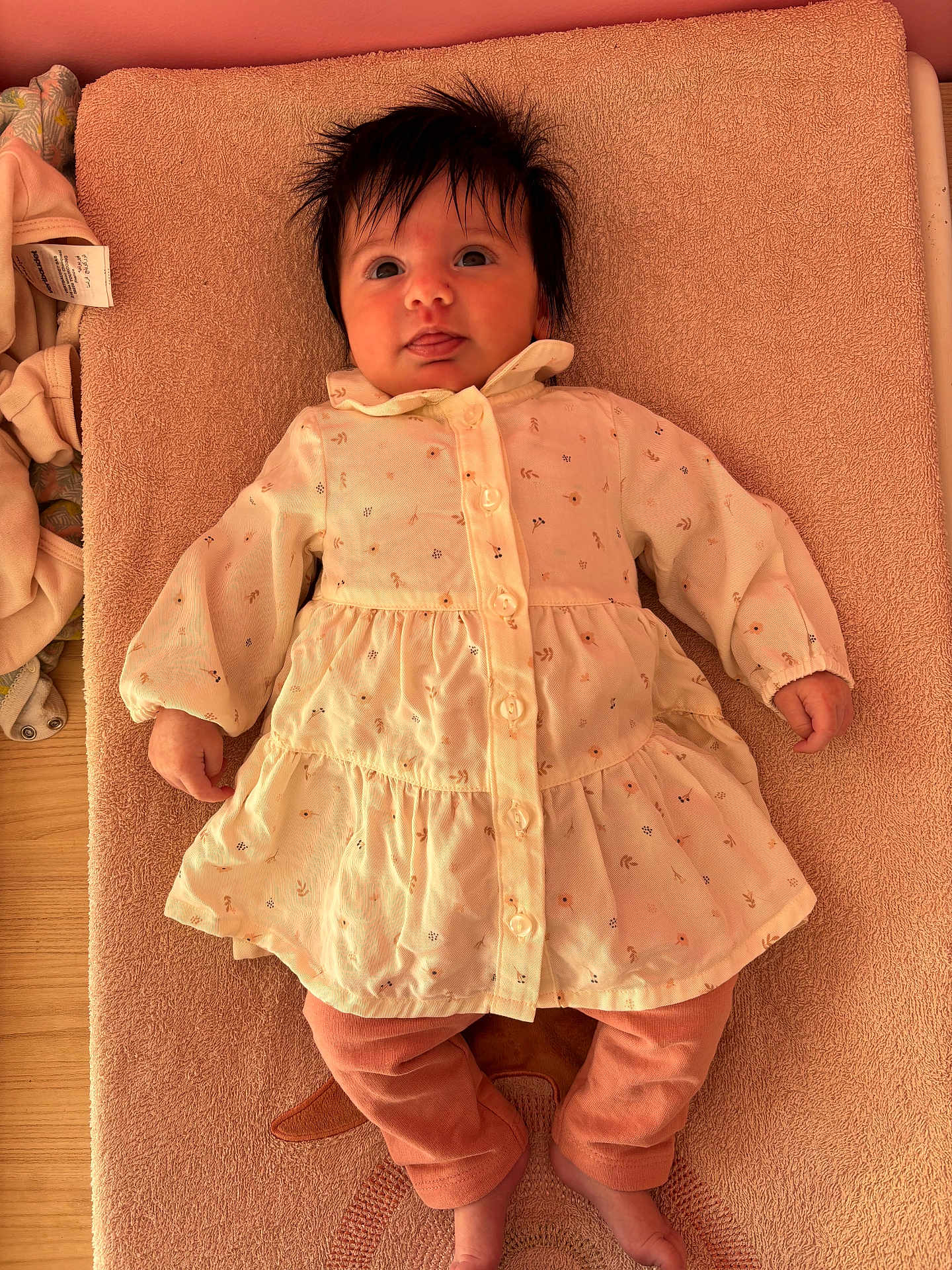 Iris a rejoint le concours — aidez-le/la à gagner de superbes lots ! baby, infant, child, towel, dress, clothing, pink_pants, floral_pattern, lying_down, tongue_out, hair, cute, indoor, wooden_surface, face, skin, hand, foot, fabric, soft_texture