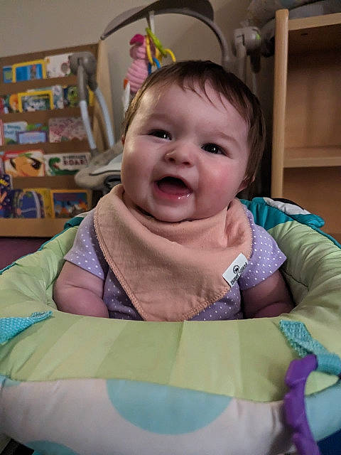 Genevieve is registered to the contest to win money with this photo: baby, baby_products, baby_safety, baby_toddler_clothing, baby_toys, bib, cheek, child, comfort, fashion_accessory, fun, happy, head, laugh, linens, person, room, sitting, smile, toddler
