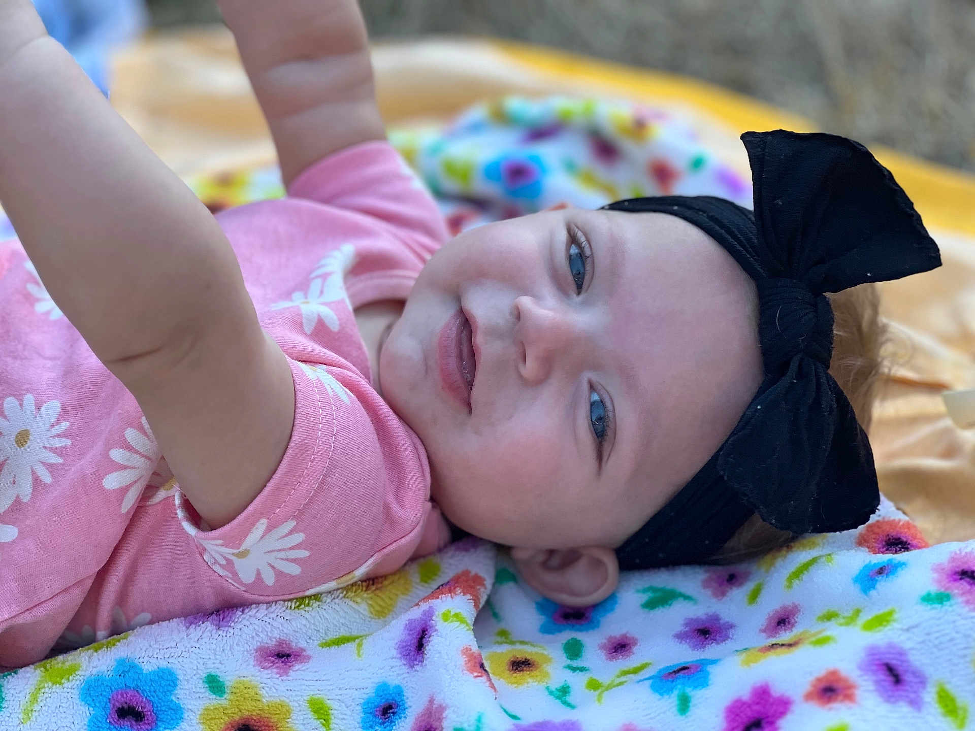 Xzanna joined the competition — help win amazing prizes! baby, child, infant, pink_clothing, black_headband, bow, face, smile, blue_eyes, blanket, floral_pattern, colorful, cute, playful, outdoor, portrait, happy, skin, head, lying_down