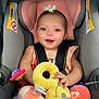 baby, car_seat, child, smiling, toy, plush_toy, pink, gray, white_bow, colorful_pants, infant, happy, cute, seatbelt, playful, feet, blue_eyes, indoors, holding, young_child