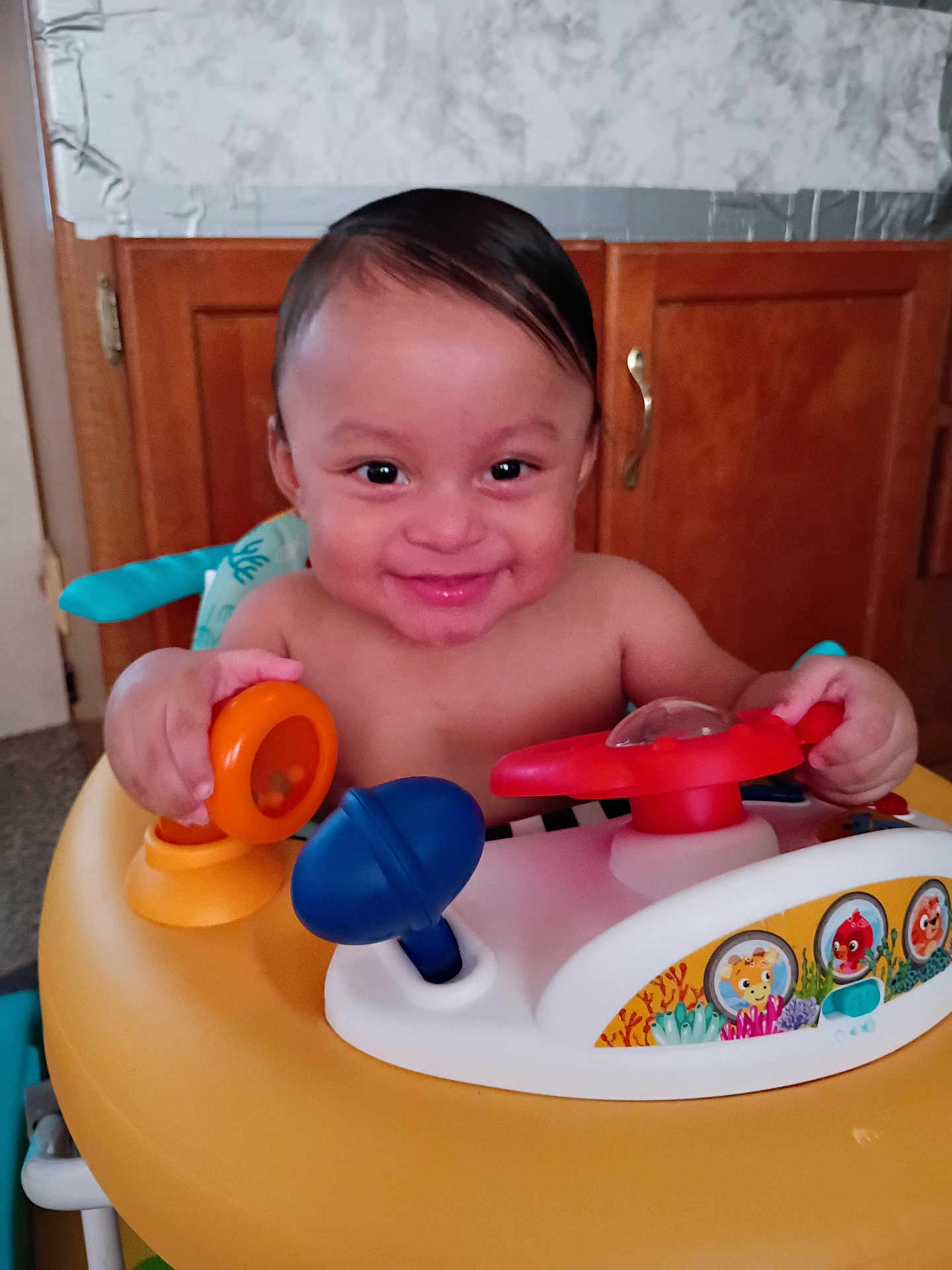 Ozias is registered to the contest to win money with this photo: baby, child, smile, happy, toy, activity_walker, indoor, kitchen, wooden_cabinet, colorful, play, person, infant, young_child, face, hands, bright, cute, joyful, home
