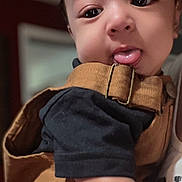 Ezekiel is registered to the contest to win money with this photo: baby, infant, child, portrait, close_up, face, wide_eyes, tongue_out, smiling, indoor, warm_lighting, brown_clothing, dark_shirt, buckle, strap, adult_hand, holding, cute, selfie, family