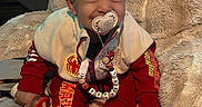 Ezekiel is registered to the contest to win money with this photo: baby, infant, child, portrait, smiling, pacifier, seated, red_outfit, jacket, sweater, socks, blanket, fluffy_blanket, cushion, bed, indoors, clothing, beaded_necklace, happy, closeup