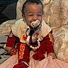 baby, infant, child, portrait, smiling, pacifier, seated, red_outfit, jacket, sweater, socks, blanket, fluffy_blanket, cushion, bed, indoors, clothing, beaded_necklace, happy, closeup