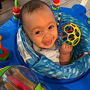 Legend is registered to the contest to win money with this photo: baby, child, infant, smiling, happy, portrait, face, eyes, hand, toy, ball, activity_center, playtime, blue, colorful, indoor, floor, seated, baby_bouncer, cheerful