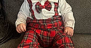 Elias is registered to the contest to win money with this photo: baby, bow_tie, child, couch, cute, expression, face, fashion, footwear, hat, indoors, person, plaid, portrait, red, sitting, slippers, texture, white_shirt, young