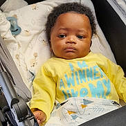 Ngom a rejoint le concours — aidez-le/la à gagner de superbes lots ! baby, infant, stroller, yellow_shirt, blanket, pacifier, face, child, indoor, expressionless, clothing, curly_hair, person, baby_bed, fabric, comfort, cute, resting, portrait, toddler
