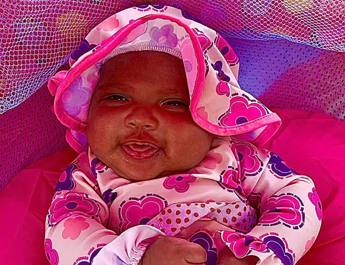 Sage joined the competition — help win amazing prizes! baby, infant, smiling, face, clothing, hat, pink, purple, floral_pattern, mesh_fabric, cute, child, portrait, happy, indoor, closeup, person, warm, cozy, playful