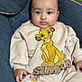 David is registered to the contest to win money with this photo: baby, child, infant, person, face, clothing, sweatshirt, pants, simba, lion_king, cartoon, illustration, seat, chair, quilted, comfortable, indoor, portrait, cute, young