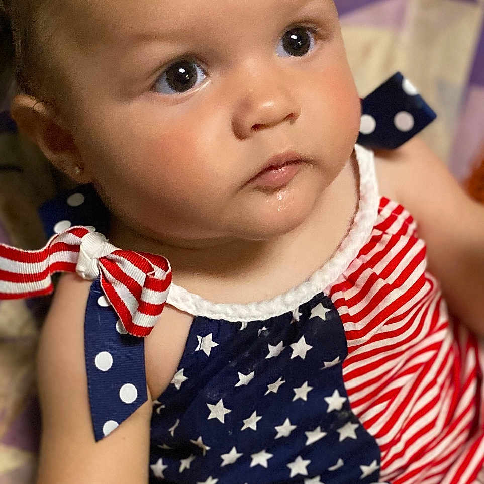 Heavenly is registered to the contest to win money with this photo: accessories, americanflag, baby, clothing, costume, couch, dress, face, flag, formalwear, frown, furniture, head, headband, person, photography, portrait, sad, sitting, tie