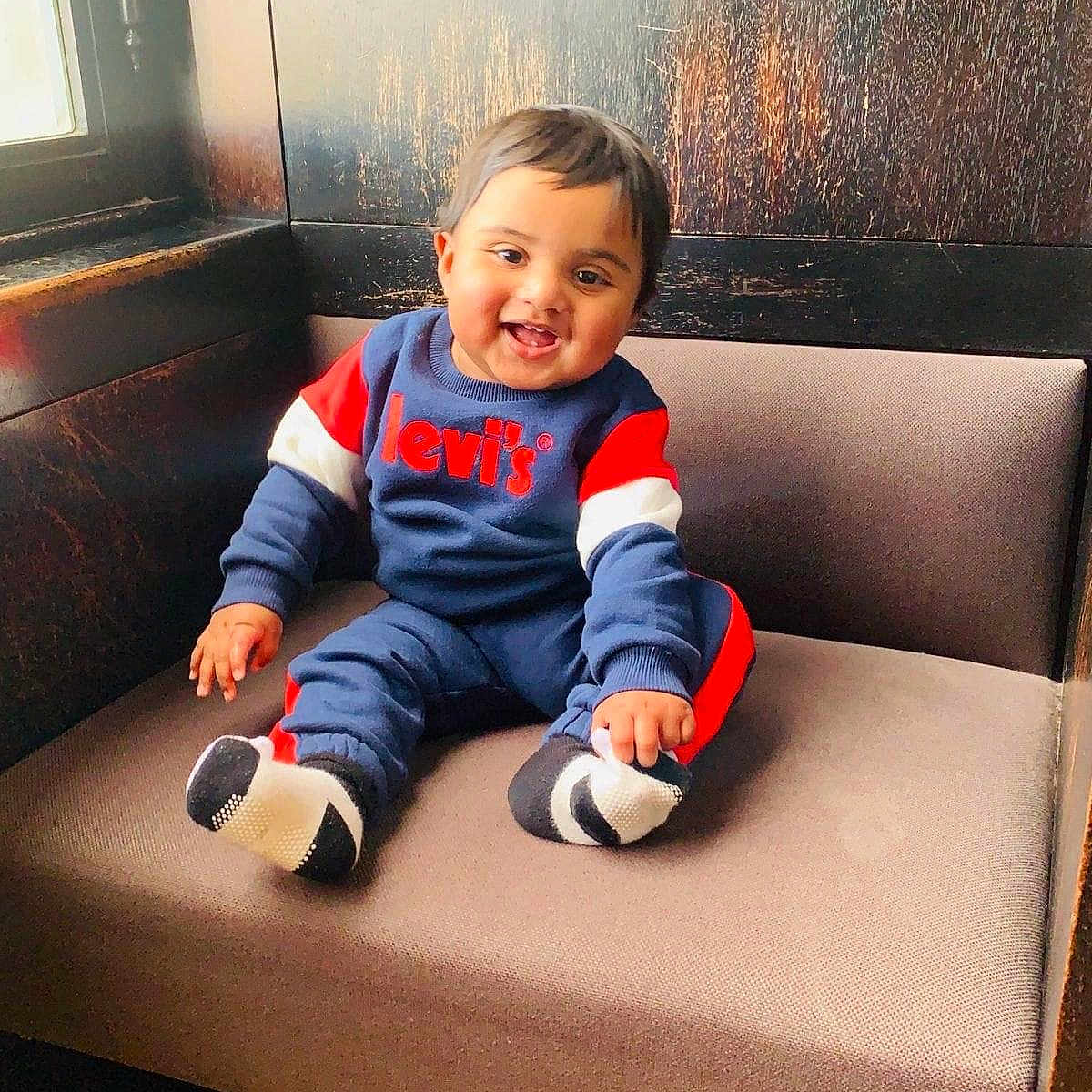 Mir is registered to the contest to win money with this photo: baby, bench, child, clothing, cozy, cushion, cute, face, footwear, happy, indoor, levis, natural_light, person, portrait, sitting, smiling, sock, window, wood