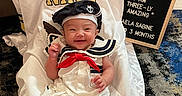 Kaela Sabine is registered to the contest to win money with this photo: baby, baby_pose, carpet, couch, cute, flag_patch, floor_rug, happy, indoor, infant, letter_board, military_theme, navy_jersey, navy_patch, portrait, sailor_hat, sailor_outfit, smile, socks, white_dress
