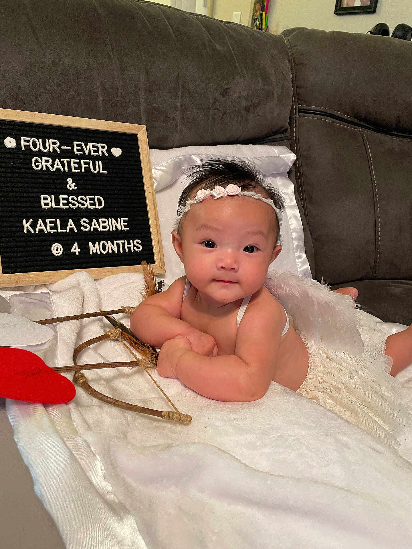 Kaela Sabine joined the competition — help win amazing prizes! baby, infant, four_months, headband, angel_wings, letter_board, heart_prop, bow_and_arrow, blanket, couch, portrait, indoor, tulle_skirt, cute, smiling, eyes, hands, props, soft_lighting, decor