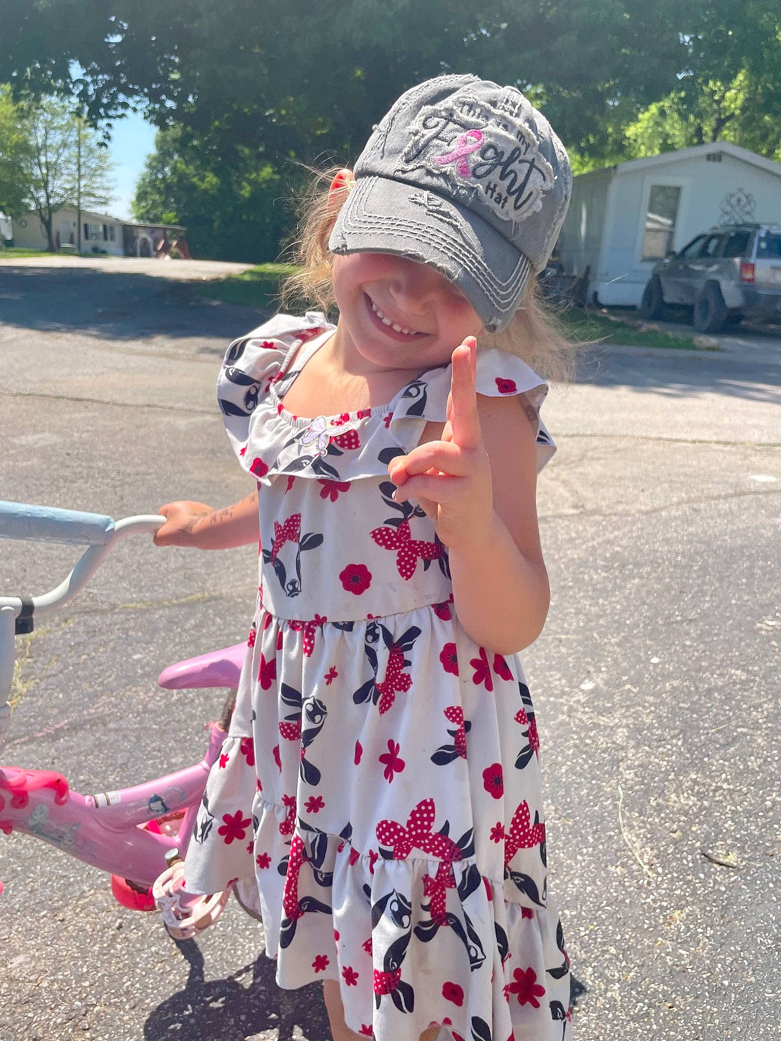 Ember is registered to the contest to win money with this photo: asphalt, baseball_cap, cap, dress, happy, hat, headgear, headwear, joy, leisure, person, pink, plant, public_space, recreation, sleeve, smile, summer, tire, toddler