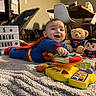 baby, infant, child, superhero, superman_costume, cape, smiling, happy, portrait, tummy_time, toy, musical_toy, teddy_bear, stuffed_animal, indoor, living_room, rug, playtime, five_months, lightbox_sign