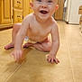 baby, crawling, kitchen, floor, smiling, diaper, child, wooden_cabinets, refrigerator, magnets, photos, tile_floor, happy, indoor, person, candid, cute, young_child, tongue_out, hands
