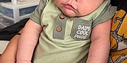 Jasper is registered to the contest to win money with this photo: baby, infant, child, person, onesie, green_clothing, hand, adult_hand, face, portrait, indoor, cozy_room, furniture, casual_clothing, cute, chubby_cheeks, sitting, holding, skin, closeup