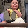 baby, stroller, child, smiling, tongue_out, yellow_clothing, blanket, seatbelt, cute, indoor, person, happy, face, head, hand, fabric, comfort, infant, playful, seat