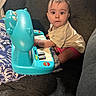 baby, child, toy, piano, blue, dinosaur, couch, blanket, cushion, indoor, curious, playing, clothing, person, infant, seated, furniture, expression, young, cute