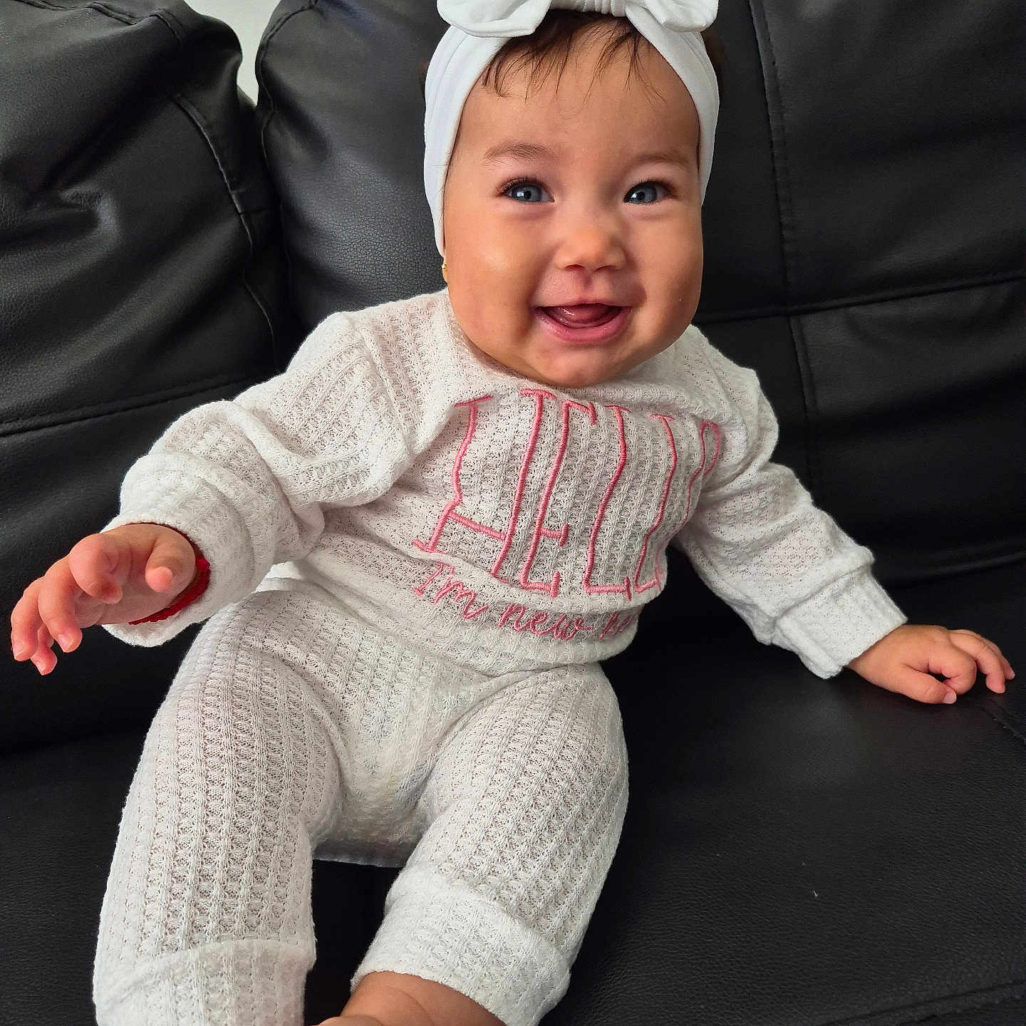 Aisha Hechvarria joined the competition — help win amazing prizes! baby, bow, child, couch, cozy, cute, expression, feet, hands, happy, headband, indoors, infant, knitwear, leather, person, portrait, sitting, smiling, white_outfit