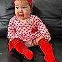baby, child, infant, red_headband, red_socks, pink_dress, hearts_pattern, sitting, black_couch, cute, happy, portrait, indoor, head_accessory, footwear, person, small_child, toddler, smile, fashion