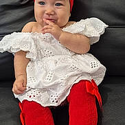 Aisha Hechvarria joined the competition — help win amazing prizes! baby, child, red_bow, headband, white_dress, red_socks, couch, leather, sitting, cute, playful, finger_near_mouth, portrait, indoors, fashion, smiling, happy, infant, clothing, person