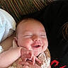 baby, smile, hands, blanket, face, infant, sleeping, person, closeup, cute, clothing, resting, skin, head, cheeks, pattern, striped_background, black_shirt, red_text, cozy
