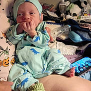 Desmond joined the competition — help win amazing prizes! baby, newborn, infant, child, portrait, sitting, pajamas, dinosaur_pattern, mint_green, baby_hat, hand, finger, smiling, bed, blanket, stuffed_animal, toy, smartphone, indoor, nursery