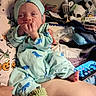 baby, newborn, infant, child, portrait, sitting, pajamas, dinosaur_pattern, mint_green, baby_hat, hand, finger, smiling, bed, blanket, stuffed_animal, toy, smartphone, indoor, nursery