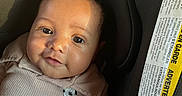 Mason is registered to the contest to win money with this photo: baby, infant, child, car_seat, portrait, face, smiling, eyes, indoor, vehicle, sunlight, shadow, clothing, onesie, mickey_mouse, cartoon, seated, close_up, safety_label, photography
