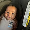 baby, infant, child, car_seat, portrait, face, smiling, eyes, indoor, vehicle, sunlight, shadow, clothing, onesie, mickey_mouse, cartoon, seated, close_up, safety_label, photography