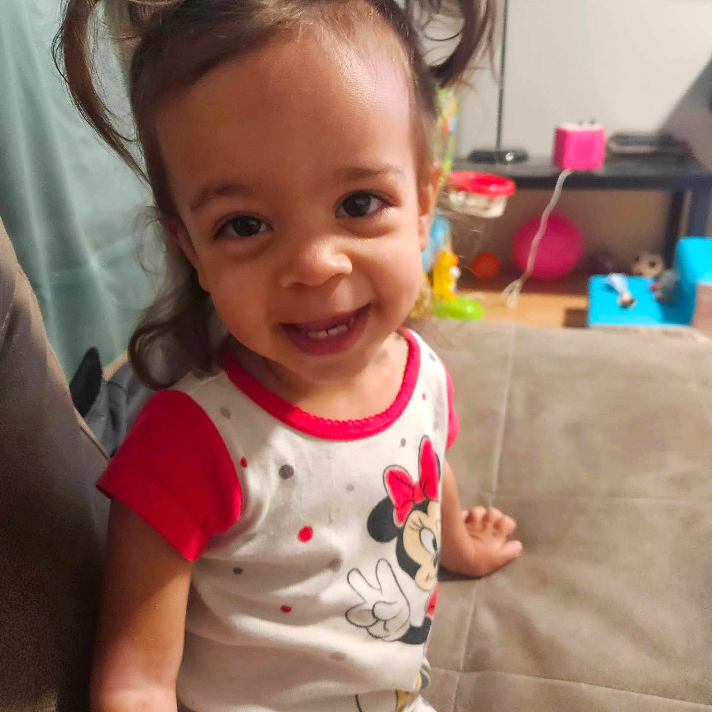 Allison is registered to the contest to win money with this photo: background, casual, child, clothing, couch, cute, face, furniture, happy, home, indoor, minnie_mouse, person, pigtails, playful, sitting, smiling, toddler, toy, young_child