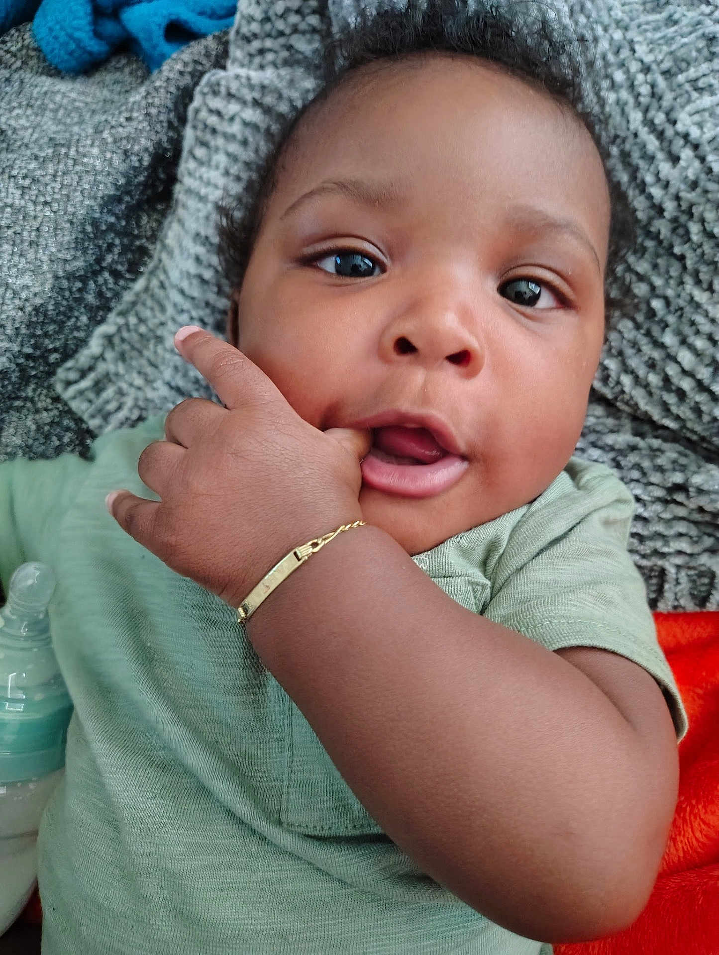 Tahjae is registered to the contest to win money with this photo: baby, infant, hand, face, eyes, clothing, bracelet, finger, bottle, blanket, texture, green_shirt, cute, closeup, skin, portrait, child, indoors, soft, expression