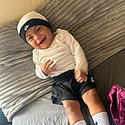 Niko is registered to the contest to win money with this photo: baby, child, smiling, laughing, nike, hat, shorts, socks, bed, blanket, pillow, plush, indoors, happy, person, clothing, footwear, cozy, home, casual