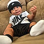 Niko is registered to the contest to win money with this photo: baby, child, nike, hat, shirt, shorts, socks, couch, furniture, indoor, person, face, expression, footwear, headwear, clothing, relaxing, seated, curious, portrait