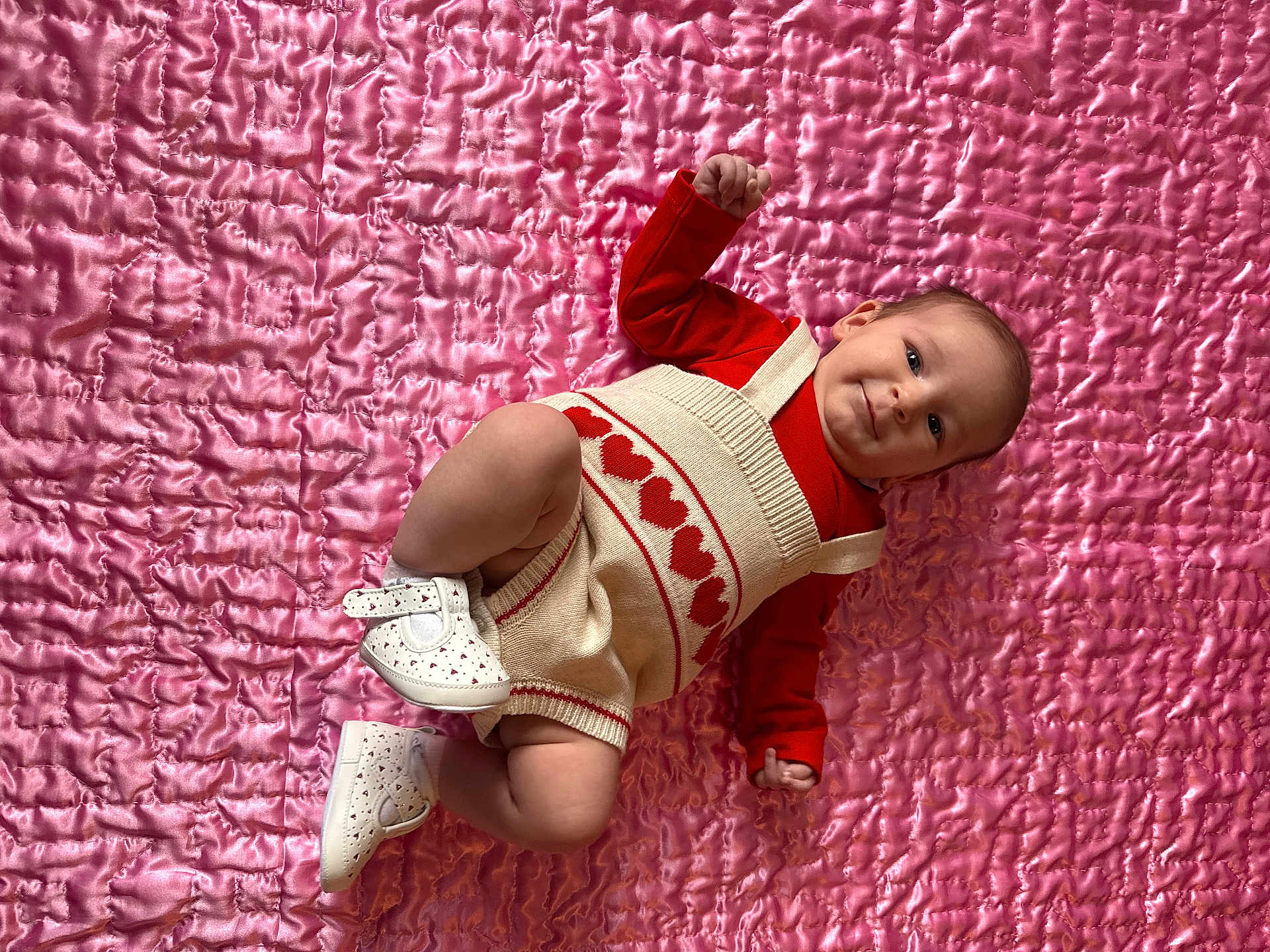 Scarlett joined the competition — help win amazing prizes! baby, infant, child, lying_down, romper, red_clothing, white_shoes, heart_pattern, pink_quilt, cute, smiling, portrait, indoor, soft_texture, happy, small_footwear, baby_fashion, closeup, adorable, infant_face