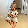 toddler, child, indoor, floor, knit_clothing, palm_tree_pattern, sitting, curious_expression, ponytail, barefoot, bracelet, door, wall, tile_floor, light, portrait, person, young_child, cute, casual