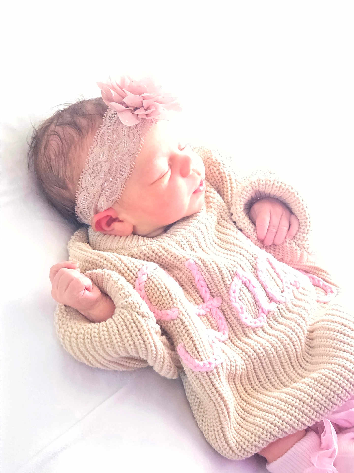 Hadley is registered to the contest to win money with this photo: newborn, baby, sleeping, knitted_sweater, headband, flower, pink, hand, soft_lighting, white_background, infant, cute, portrait, peaceful, cozy, warm_clothing, child, resting, indoors, baby_girl