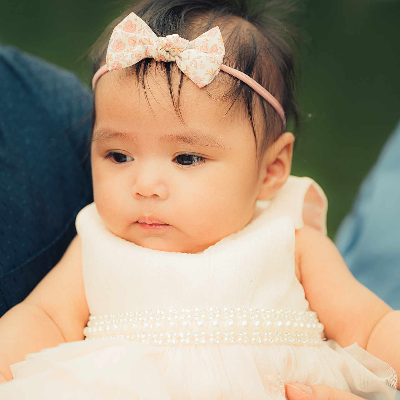 Maria Arya is registered to the contest to win money with this photo: baby, bow, calm, child, cute, dress, face, girl, hair, hand, headband, holding, infant, outdoor, pearl, person, portrait, skin, soft_focus, white_dress