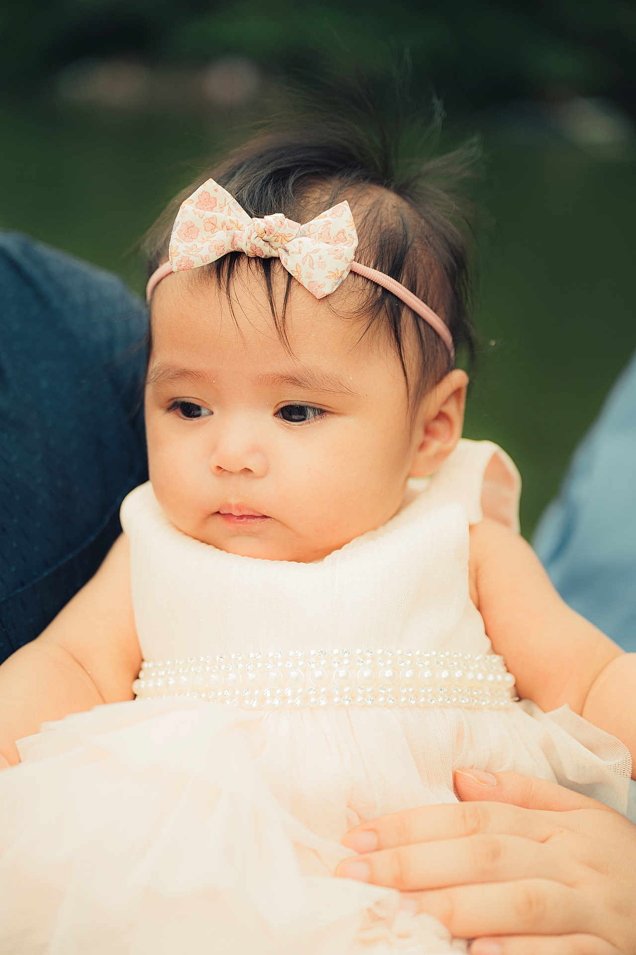 Maria Arya is registered to the contest to win money with this photo: baby, child, girl, dress, headband, bow, pearl, white_dress, portrait, face, hand, skin, hair, outdoor, soft_focus, person, cute, infant, holding, calm