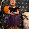 backdrop, beads, boots, child, couch, decor, festive, floor, girl, halloween, happy, holiday, indoor, person, pumpkin, purple_dress, smiling, spider_web, toy, wooden_floor