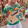 Emersyn is registered to the contest to win money with this photo: child, girl, smiling, preschool, sign, backpack, pigtails, white_shoes, outdoor, plants, sidewalk, green_shirt, white_skirt, happy, celebration, daycare, cute, person, school, first_day