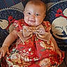 baby, bow, child, clothing, colorful, couch, cute, fabric, face, floral_pattern, happy, indoor, infant, person, portrait, quilt, red_dress, seated, smiling, young