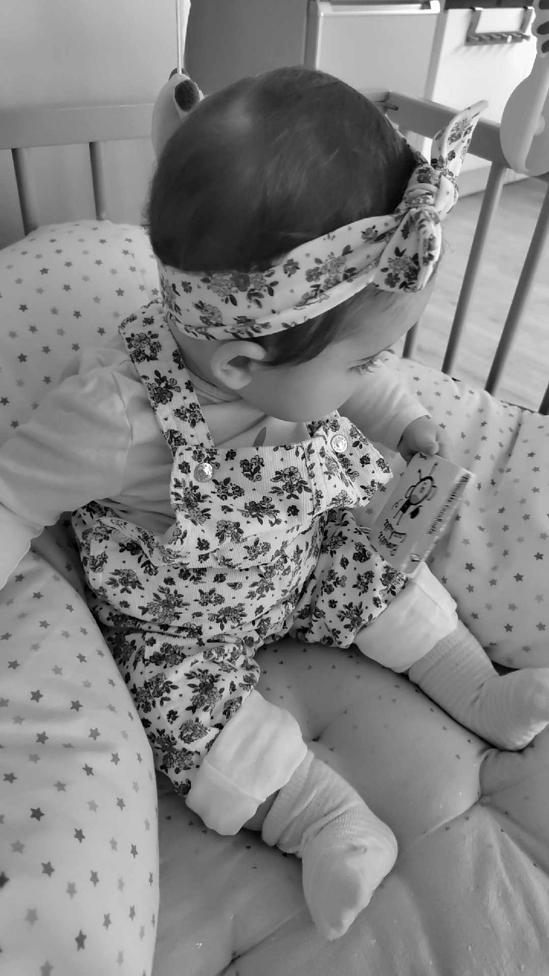 Loumïa participe au concours pour gagner de l'argent avec cette photo : baby, infant, child, crib, cushion, headband, floral, overalls, socks, book, cartoon, bee, pattern, stars, black_and_white, seated, soft_toys, hand, floor, indoors