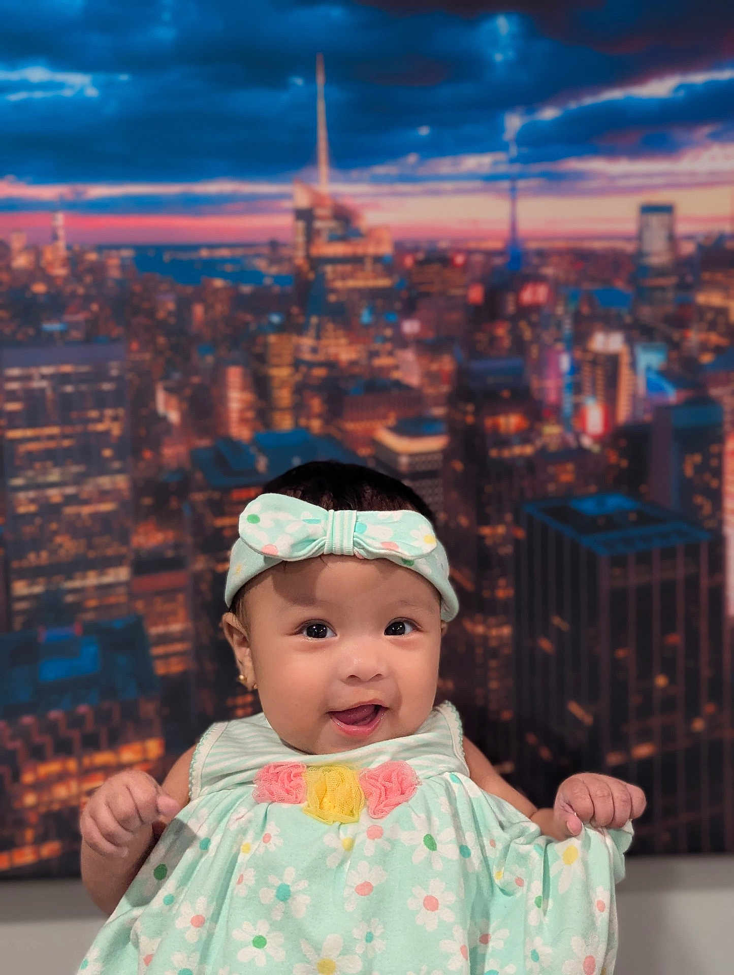 Aaliyah is registered to the contest to win money with this photo: baby, child, smiling, headband, dress, floral_pattern, indoor, portrait, cute, happy, infant, cityscape, background, girl, person, fashion, accessory, skin, face, expression