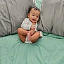 baby, smiling, onesie, bed, pillow, gray_pillow, mint_green_bed, infant, cute, happy, child, foot, hand, indoors, playful, sitting, face, person, cozy, soft